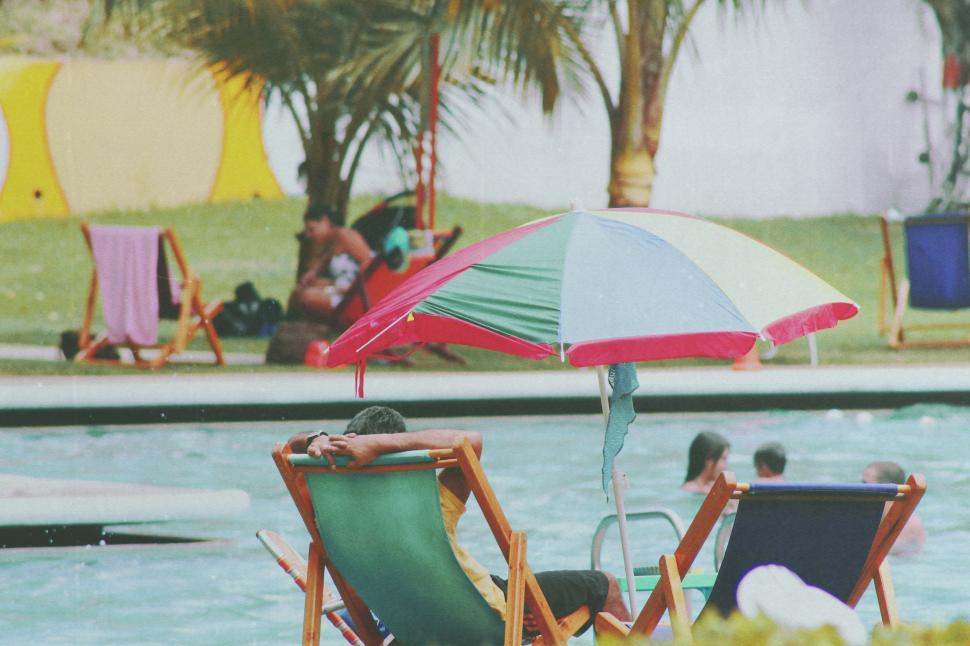 People enjoying summer day at the swimming pool View of deck chairs and umbrella with people in swimming pool